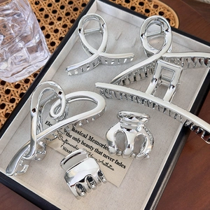 Five-piece silver metallic heart hair claw set for bun hairstyles on a beige tray