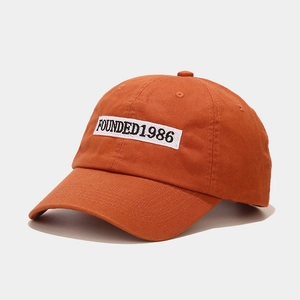 Close-up of orange cotton baseball cap featuring the white 1986 embroidery patch