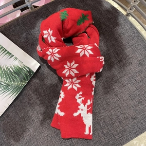 Detail of red Christmas knit scarf featuring white snowflakes, elk, and green tree patterns