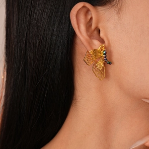 Close-up of model wearing gold hollow butterfly earrings with colored beaded accents