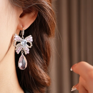 Close-up of pink bow drop earrings with tassels worn by a model in soft lighting
