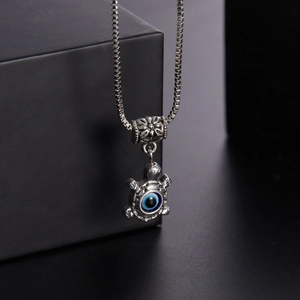 Detail of silver box chain necklace with turtle evil eye pendant on a dark pedestal