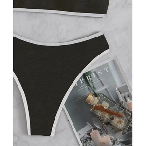 Dettaglio slip bikini nero a vita alta con bordo bianco e tessuto a trama ondulata