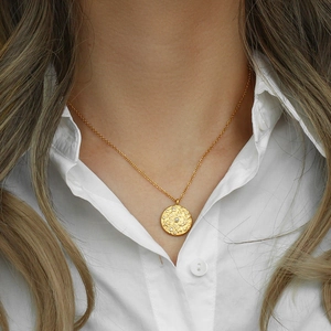Dettaglio di una collana con ciondolo a moneta d'oro con stella, luna e zirconi incastonati