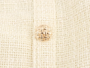 Nahaufnahme eines goldenen Metallknopfs auf cremefarbenem Tweed-Stoffkleid