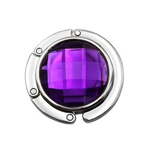 Close-up of folding purse hook with a large purple faceted gemstone and silver frame