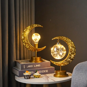 Détail de lampe lune dorée avec ampoule LED et motifs ajourés sur table en marbre blanc