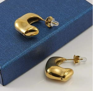 Détail macro de boucles d'oreilles dorées irrégulières sur un écrin bleu de luxe