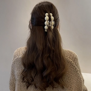 Détail d'une grande pince à cheveux élégante en perles sur cheveux ondulés marron