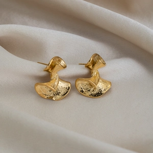 Gros plan de boucles d'oreilles en éventail dorées à texture martelée sur tissu beige