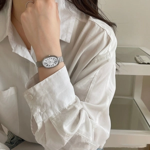 Detail of elegant silver steel watch with white oval dial on female wrist wearing a shirt
