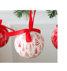 White Christmas ball with red tree patterns and a silk bow hanging on a green tree branch