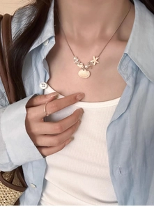 Close-up of ocean-themed necklace with shell and starfish charms on a light blue shirt