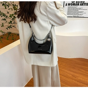 Side view of a black patent leather crescent bag with silver ball charm on model