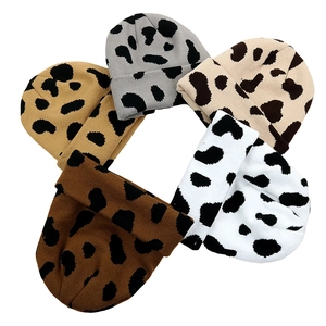 Top view of five knitted beanies featuring leopard and cow patterns in various earth tones