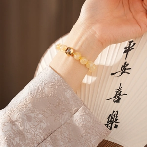Close-up of yellow citrine gourd bracelet on wrist with elegant traditional fan background