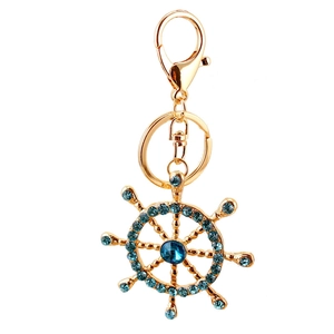 Golden ship wheel keychain featuring blue crystals and sparkling rhinestones on white background