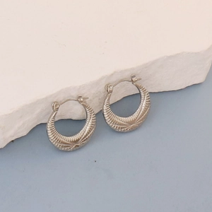 Detailed view of silver oval hoop earrings with retro etched textures on white stone