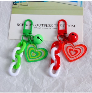 Detail of red and green heart keychains with acrylic chains and bells on white background