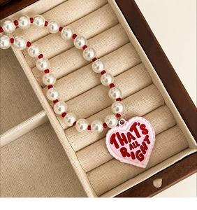 Detail of beaded pearl necklace featuring a pink heart pendant with lettered engraving