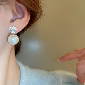 Close-up of elegant pearl drop earrings with zircon studs worn by a model in warm light