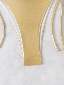 Detail shot of shimmering gold metallic bikini bottom with side strings and lining