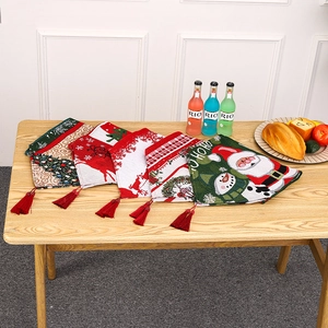 Christmas table runner with Santa and reindeer patterns and red tassel on wooden desk