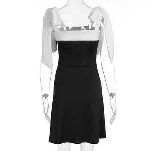 Detail of elegant black dress featuring large white bow-tie straps and slim fit pleats