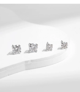 Macro detail of four sparkling round moissanite silver stud earrings on a white podium