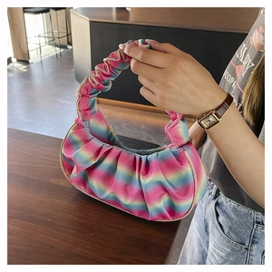 Detailed view of a rainbow pleated satin handbag held by a model in a cafe setting