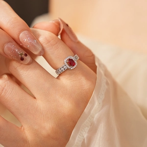 Macro view of silver ring with red oval gemstone and pavé white zircons on model finger