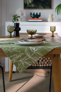 Macro shot of green cotton linen table runner with white leaf patterns on a wooden table