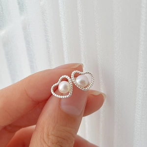 Close-up of hollow heart stud earrings with white pearl detail in silver finish