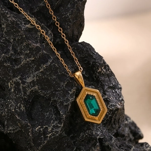 Detail view of a 18K gold-plated hexagonal necklace with emerald stone on a rock