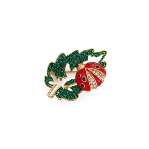 Detailed macro shot of a golden ladybug brooch with green crystals on a hollowed leaf