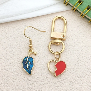 Detail of blue leaf earrings and red heart keychain charms on textured surface