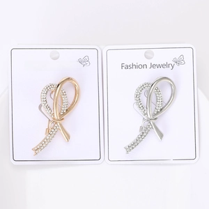 Detailed close-up of gold and silver ribbon brooches with crystal pavé on white cardboards