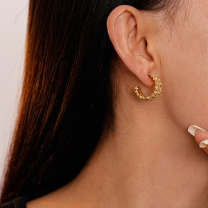Close-up of a gold-plated C-shaped earring with textured zircon on a model's ear