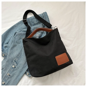 Detail of black canvas tote bag with brown leather handles and adjustable shoulder strap