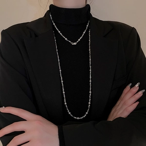 Vue détaillée d'un collier à perles argentées superposé sur un pull noir élégant