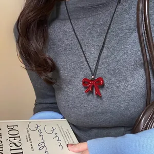 Close-up of a red enamel bow pendant necklace on a black leather cord worn by a model