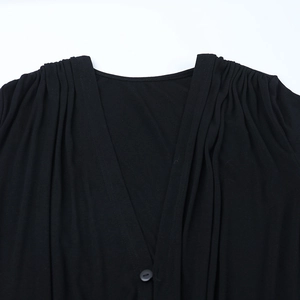 Detailed view of black V-neck dress with shoulder pleats and single button closure