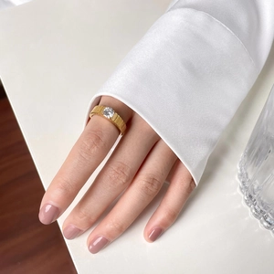 Close-up of golden gear-style ring with a round diamond on a model's finger