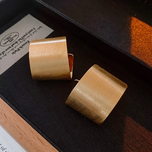 Detailed macro view of matte gold brushed metal wide earrings on a vintage tray