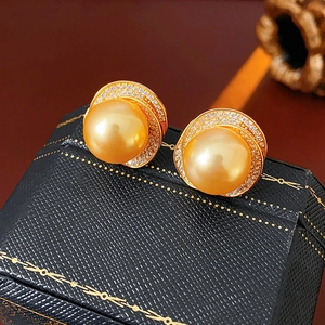 Detailed view of golden pearl stud earrings with sparkling zircon accents on jewelry box
