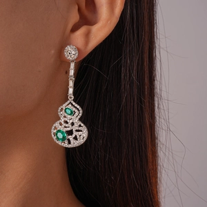 Détail de boucles d'oreilles argentées en forme de gourde avec pierres vertes et diamants