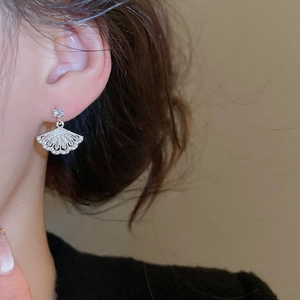 Macro side view of silver fan-shaped earring with zircon on model's ear detail