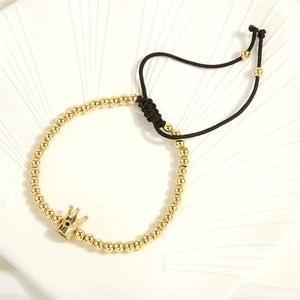 Macro detail of gold beaded bracelet featuring crown charm and black adjustable cord