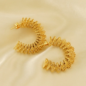 Detailed close-up of gold twist texture earrings on elegant pale yellow silk background