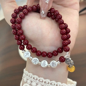 Detail of red bead double bracelet with engraved silver charm and yellow crystal accent